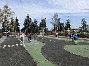 Dzieci uczestniczą w zajęciach edukacyjnych na miasteczku ruchu drogowego na świeżym powietrzu.