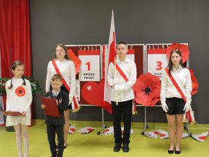 Uczniowie w strojach galowych wchodzący w skład pocztu flagowego szkoły stoją z flagą Polski podczas części oficjalnej apelu.