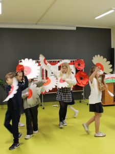 Dzieci prezentują choreografię, unosząc papierowe kwiaty w barwach Polski.