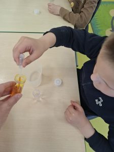 Dziecko wykonuje doświadczenie z użyciem pipety i barwionej cieczy podczas zajęć edukacyjnych.