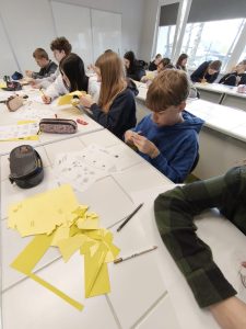 Grupa uczniów w klasie skupiona na pracy plastycznej – wycinaniu i składaniu żonkili z papieru według instrukcji.