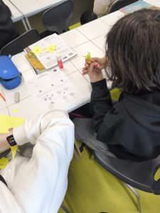 Uczeń trzyma w dłoni gotowego papierowego żonkila, obok leżą materiały instruktażowe i przybory szkolne.