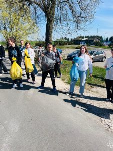 Grupa uczniów idzie poboczem drogi, niosąc worki z zebranymi odpadami po sprzątaniu okolic szkoły w ramach obchodów Dnia Ziemi.