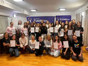 Grupa uczniów klasy 8 z nauczycielami pozuje z certyfikatami podczas obozu językowego EuroWeek w sali szkoleniowej.