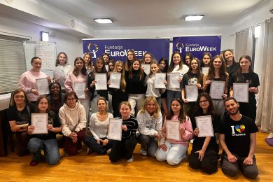 Grupa uczniów klasy 8 z nauczycielami pozuje z certyfikatami podczas obozu językowego EuroWeek w sali szkoleniowej.