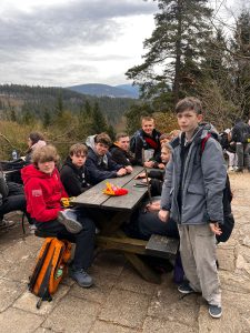 Uczniowie siedzą przy drewnianym stole na zewnątrz w górach podczas wycieczki w trakcie obozu EuroWeek.