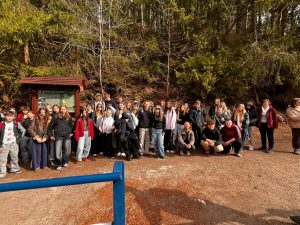 Grupa uczniów klasy 8 z opiekunami stoi na leśnej ścieżce przy tablicy informacyjnej podczas wycieczki.