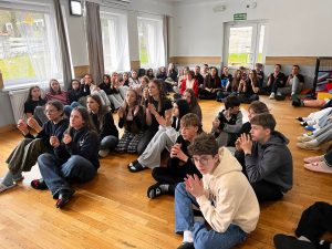 Uczniowie siedzą na podłodze w sali i słuchają prowadzącego podczas zajęć integracyjnych.