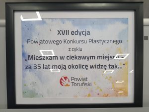 Plansza informacyjna XVI Powiatowego Konkursu Plastycznego z tytułem wydarzenia i logotypem Powiatu Toruńskiego.