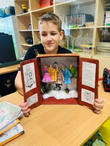 Uczeń prezentuje makietę szafy z ubraniami i elementami świata Narnii przygotowaną na podstawie lektury.