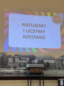 Slajd z napisem „Ratujemy i Uczymy Ratować” wyświetlany podczas prezentacji programu pierwszej pomocy.