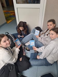 Uczennice siedzą na korytarzu i czytają materiały informacyjne o autyzmie podczas szkolnych obchodów dnia świadomości autyzmu.