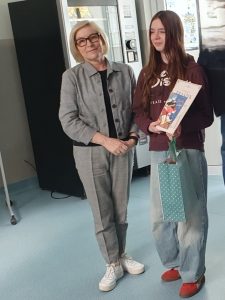 Uczennica prezentuje otrzymaną książkę i torbę z nagrodą za udział w konkursie na fraszkę.