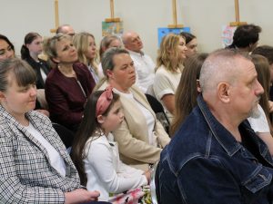 Uczestnicy i goście obserwują przebieg gali oraz występy konkursowe. Na ścianach widoczne są prezentowane prace plastyczne.