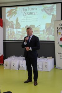 Wystąpienie przedstawiciela władz samorządowych podczas gali rozdania nagród. W tle widoczna prezentacja poświęcona Janowi Marcinowi Szancerowi.