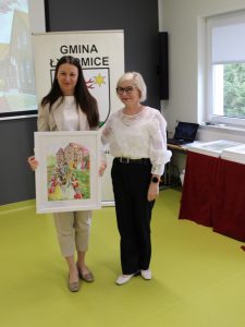 Pamiątkowe zdjęcie przedstawicielek organizatorów z oprawioną pracą inspirowaną twórczością Jana Marcina Szancera.