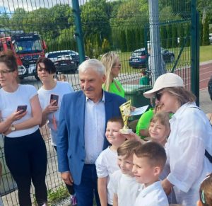 Przedstawiciele oddziału przedszkolnego SP w Ostaszewie odbierają puchar za zajęcie I miejsca w VIII Olimpiadzie Przedszkolaka „Jelonki na start”. Dzieci pozują do zdjęcia wraz z organizatorami i zaproszonymi gośćmi.