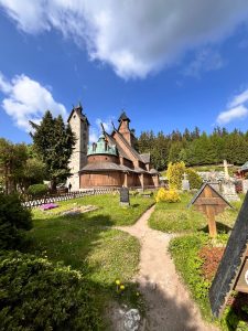 Widok na drewnianą Świątynię Wang w Karpaczu otoczoną zielenią. Na pierwszym planie znajduje się zabytkowy cmentarz przykościelny.