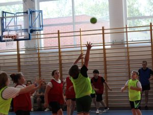 Fragment meczu piłki ręcznej. Uczniowie w czerwonych i zielonych znacznikach walczą o piłkę podczas rozgrywek sportowych.