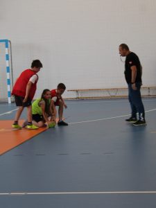 Nauczyciel wychowania fizycznego nadzoruje wznowienie gry podczas szkolnego turnieju piłki ręcznej.