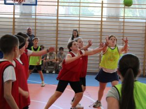 Uczennice i uczniowie próbują przejąć piłkę podczas dynamicznej akcji w meczu piłki ręcznej rozgrywanym w hali sportowej.