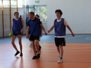 Zawodnicy drużyny w niebieskich znacznikach przemieszczają się po boisku podczas rozgrywek sportowych.