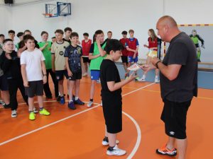 Laureat odbiera nagrodę za udział w turnieju piłki ręcznej. Pozostali uczniowie nagradzają uczestników brawami.