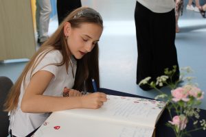 Uczennica wpisuje pamiątkowy wpis do kroniki podczas Gali Absolwentów Gminy Łysomice. Na stole znajduje się ozdobna kronika oraz wazon z kwiatami.