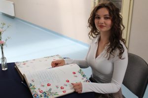 Uczennica siedzi przy kronice Gali Absolwentów Gminy Łysomice, przygotowana do wpisania pamiątkowego wpisu.