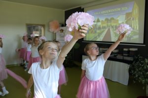Dziewczynki prezentują taniec z różowymi kwiatami podczas występu artystycznego na Gali Absolwentów Gminy Łysomice.