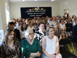 Uczestnicy Gali Absolwentów Gminy Łysomice z uwagą słuchają przemówień. W pierwszych rzędach siedzą uczniowie, rodzice i zaproszeni goście.