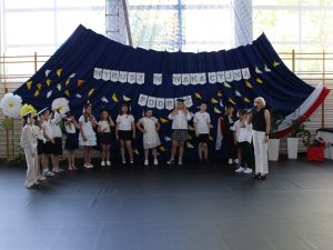 Dyrektor szkoły przemawia do uczniów klasy III podczas uroczystości zakończenia pierwszego etapu edukacyjnego. Uczniowie występują w symbolicznych biretach.
