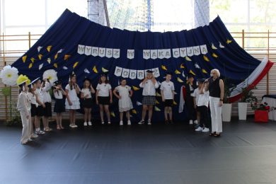 Dyrektor szkoły przemawia do uczniów klasy III podczas uroczystości zakończenia pierwszego etapu edukacyjnego. Uczniowie występują w symbolicznych biretach.