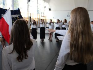 Uczniowie klasy ósmej stojący w kręgu składają ślubowanie podczas uroczystości zakończenia roku szkolnego. W centrum znajduje się poczet flagowy z flagą państwową.