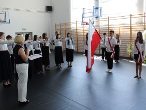 Pani dyrektor odczytuje tekst ślubowania, a uczniowie klas ósmych wyciągniętą dłonią potwierdzają jego treść podczas ceremonii pożegnania szkoły.