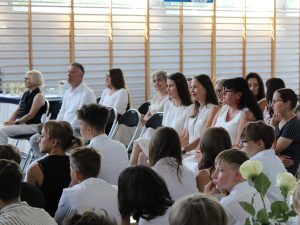 Zaproszeni goście, nauczyciele i rodzice obserwują przebieg uroczystości zakończenia roku szkolnego. Wśród uczestników znajdują się przedstawiciele władz gminy.