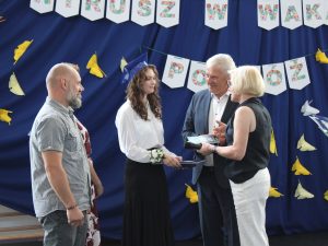 Pani dyrektor oraz Wójt Gminy Łysomice wręczają najlepszej absolwentce szkoły nagrodę i gratulacje w obecności rodziców podczas zakończenia roku szkolnego.