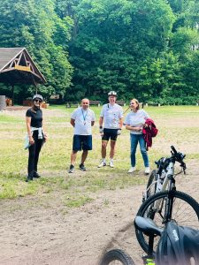 Opiekunowie rajdu rowerowego stoją na polanie przy Barbarce. W tle widoczna jest drewniana wiata i otaczający ją las, a na pierwszym planie znajdują się rowery uczestników.