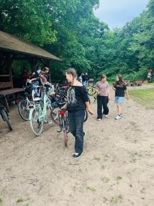 Uczennice oraz pozostali uczestnicy przygotowują się do dalszej jazdy po przerwie na Barbarce. Obok wiaty stoją liczne rowery, a wokół rozciąga się zielony teren rekreacyjny.