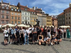 Grupa uczniów klas starszych pozuje do wspólnego zdjęcia przy Pomniku Syrenki Warszawskiej na Rynku Starego Miasta. W tle widoczne są zabytkowe kamienice.