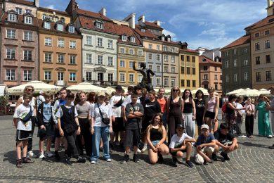 Grupa uczniów klas starszych pozuje do wspólnego zdjęcia przy Pomniku Syrenki Warszawskiej na Rynku Starego Miasta. W tle widoczne są zabytkowe kamienice.