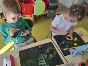 Dwoje dzieci malujących elementy z naturalnych materiałów podczas pracy nad makietą jesiennego lasu.