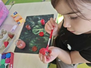 Dziewczynka malująca farbą element z kory podczas tworzenia jesiennej makiety.