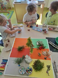 Dzieci przygotowujące elementy z plasteliny i naturalnych materiałów do wspólnej makiety jesiennego lasu.
