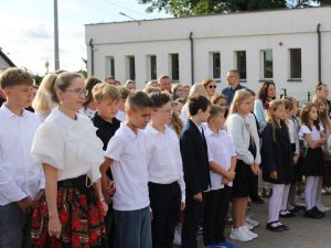 Uczniowie, nauczyciele i rodzice uczestniczący w uroczystości rozpoczęcia roku szkolnego przed budynkiem szkoły.