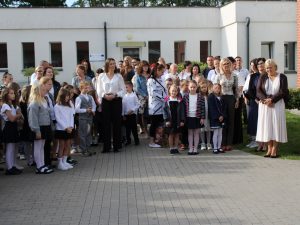 Uczniowie, nauczyciele i rodzice zgromadzeni na placu przed szkołą podczas uroczystości rozpoczęcia roku szkolnego.