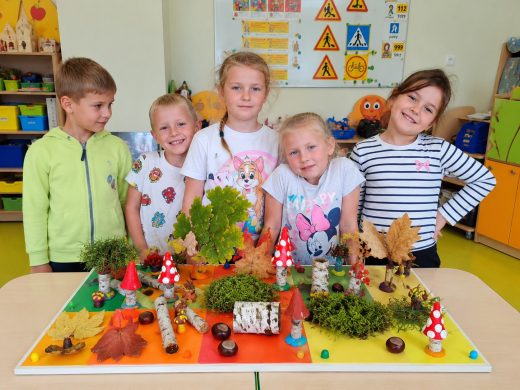 Dzieci z oddziału przedszkolnego prezentujące wykonaną wspólnie makietę jesiennego lasu.