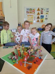Dzieci z oddziału przedszkolnego przy powstającej makiecie jesiennego lasu wykonanej z liści, mchu, kory, gałązek i plasteliny.