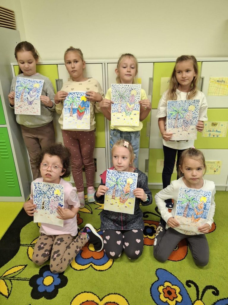 Grupa uczennic prezentuje wykonane techniką kropkowania kolorowe prace plastyczne przedstawiające palmy i deski surfingowe.