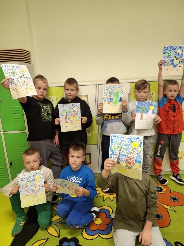 Grupa uczniów prezentuje prace plastyczne z palmami i deskami surfingowymi, wykonane techniką kropkowania z okazji Międzynarodowego Dnia Kropki.